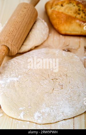 Étaler la pâte à levures sur une planche de bois. Derrière elle un rouleau de pâte et un petit pain Banque D'Images