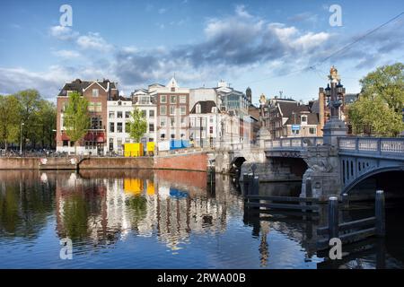 Pittoresques vieilles maisons avec des reflets sur les eaux de la rivière Amstel dans la ville d'Amsterdam, aux pays-Bas, Pont Bleu (Blauwbrug) sur la droite Banque D'Images