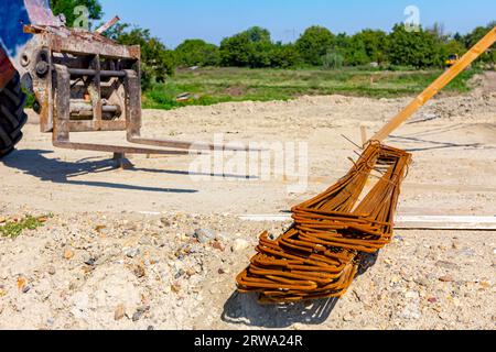 Les machines de chariot élévateur pour la livraison et le transport se préparent à soulever le paquet sélectionné d'armature rouillée du sol sur le chantier de construction. Banque D'Images