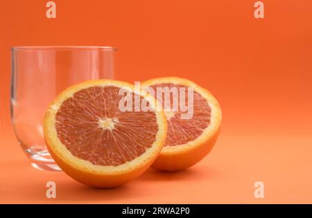 Gros plan d'un rouge orange coupé en deux à côté d'un verre sur un fond orange avec espace copie Banque D'Images
