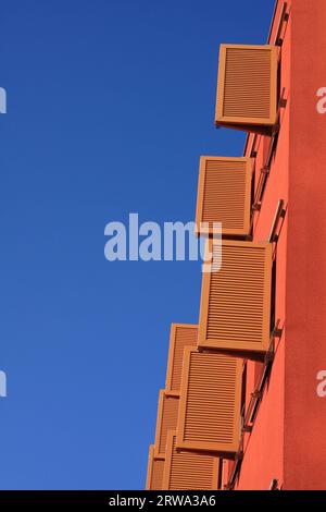 Volets ouverts bruns sur un mur de maison couleur terre cuite d'un immeuble de bureaux, fond bleu ciel, format vertical Banque D'Images