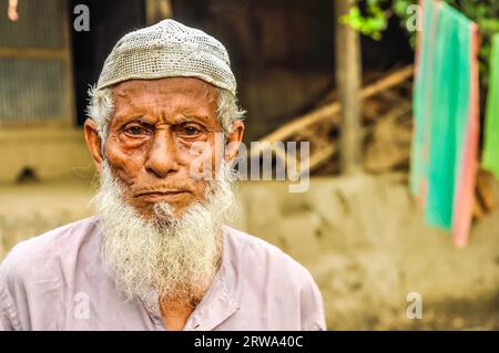 Paigacha, Bangladesh, vers juillet 2012 : un vieil homme aux cheveux blancs courts et à la longue barbe blanche porte une casquette et une chemise blanches à Paigacha, Bangladesh. Banque D'Images
