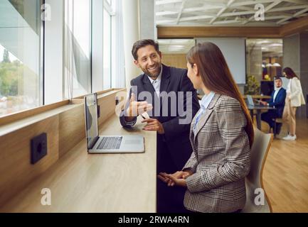 Deux collègues homme et femme discutant du projet de travail dans le bureau assis avec ordinateur portable. Banque D'Images