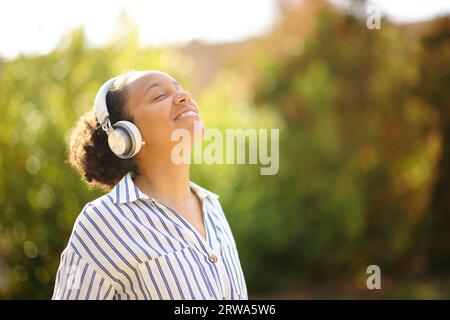 Heureuse femme noire méditant l'écoute audio guide avec casque dans un parc Banque D'Images