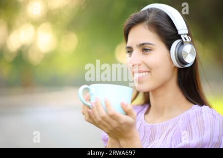 Femme heureuse écoutant de la musique buvant du café regardant loin dans un parc Banque D'Images