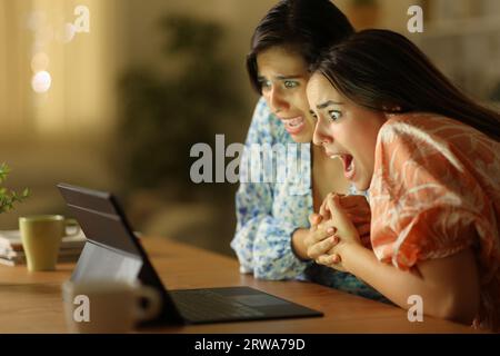 Femmes terrifiées regardant les médias sur ordinateur portable dans la nuit à la maison Banque D'Images