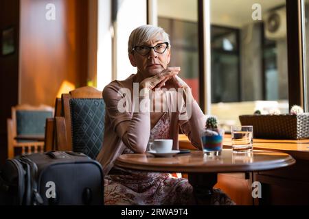Femme mature est assise dans un café à l'aéroport, attendant l'embarquement. Banque D'Images