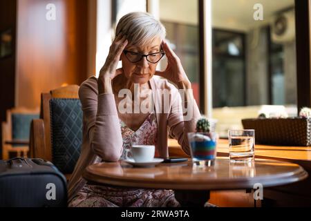 Femme mature est assise dans un café à l'aéroport, attendant l'embarquement. Banque D'Images
