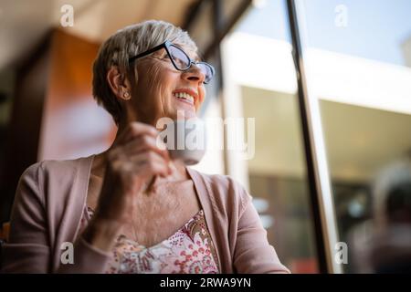 Femme mûre boit du café dans un café. Elle profite de la journée ensoleillée et se détend. Banque D'Images