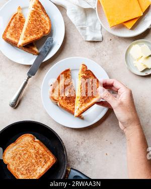 Vue de dessus de la main ramassant le sandwich au fromage grillé sur l'assiette. Banque D'Images