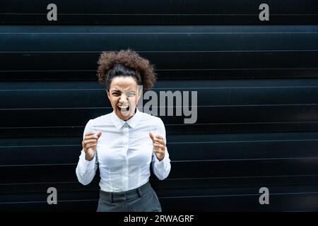 Femme stressée devient folle tirant ses cheveux dans la frustration près de la jeune femme d'affaires. Employé de bureau féminin debout contre le mur noir frustr Banque D'Images