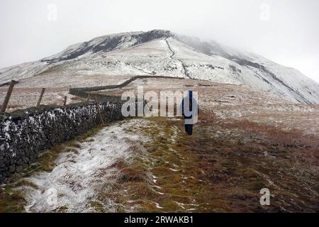 Homme marchant sur le chemin dans la neige à Ingleborough l'un des trois pics du Yorkshire, parc national des Yorkshire Dales, Angleterre, Royaume-Uni Banque D'Images