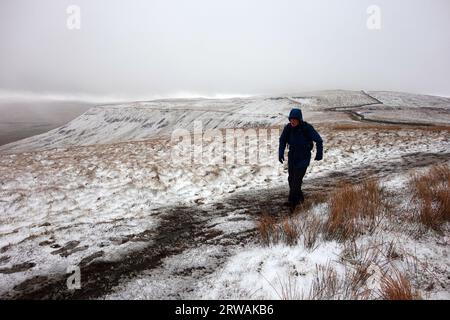 Homme marchant sur le chemin dans la neige à Ingleborough l'un des trois pics du Yorkshire, parc national des Yorkshire Dales, Angleterre, Royaume-Uni Banque D'Images