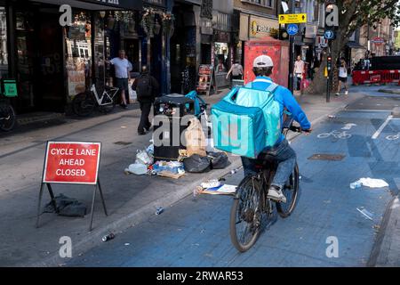 Litière cyclable Lane SuperHighway à Aldgate / Whitechapel le 16 août 2023 à Londres, Royaume-Uni. Dans cette zone, il y a souvent des poubelles débordantes et des déchets commerciaux laissés sur le trottoir. Une autoroute cyclable est une longue piste cyclable qui fait partie du réseau cyclable coordonné par TfL. C'est un itinéraire populaire auprès des cyclistes de banlieue et de loisirs, passant par un certain nombre de destinations majeures de Londres le long de son itinéraire. Sur presque tout le parcours, les cyclistes sont séparés des autres véhicules dans des voies cyclables séparées, et une infrastructure cyclable a été fournie aux principaux échangeurs. Banque D'Images