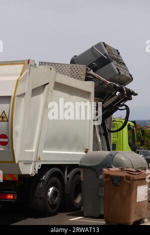 Un camion poubelle ramassant les conteneurs latéralement et automatiquement sur la rue pendant la journée Banque D'Images