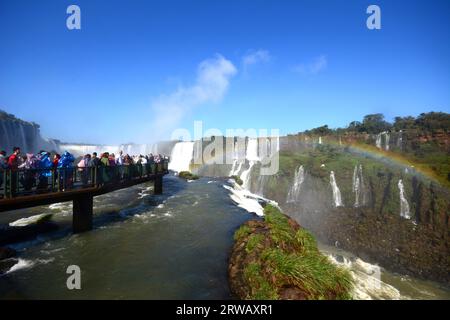 Touristes aux chutes d'Iguazu, l'une des grandes merveilles naturelles du monde, à la frontière du Brésil et de l'Argentine avec un arc-en-ciel sur la droite. Banque D'Images