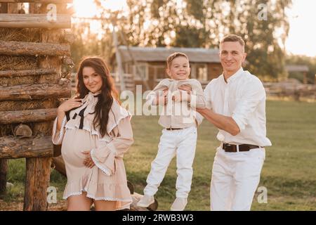 Une famille élégante dans la campagne au coucher du soleil. Une femme enceinte avec son mari et son fils dans la nature. Banque D'Images