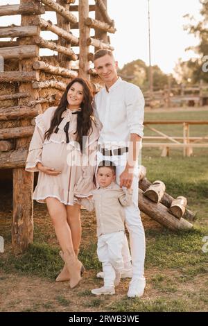 Une famille élégante dans la campagne au coucher du soleil. Une femme enceinte avec son mari et son fils dans la nature. Banque D'Images