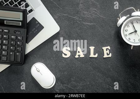 Texte en bois Vente et calculatrice sur fond texturé noir, vue de dessus. Banque D'Images