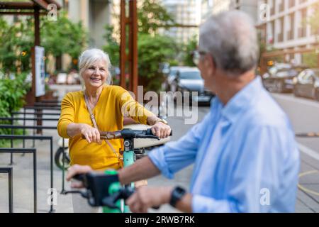 Couple senior conduisant des scooters électriques dans la ville Banque D'Images