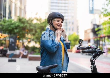 Portrait d'une femme âgée portant un casque tout en faisant du vélo dans la ville Banque D'Images