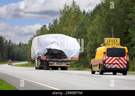 Le camion transporte une charge surdimensionnée sur une remorque à plateau vers le port de Hanko. Le transport a des véhicules pilotes à l'avant et à l'arrière. Raasepori, Finlande. 8 septembre 23 Banque D'Images