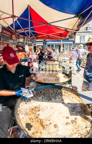 Femme travaillant sur un stand de nourriture française en plein air dans la ville de Sandwich dans le Kent. Comptoir a cinq énormes casseroles d'aliments tels que la tartiflette et la paella. Banque D'Images