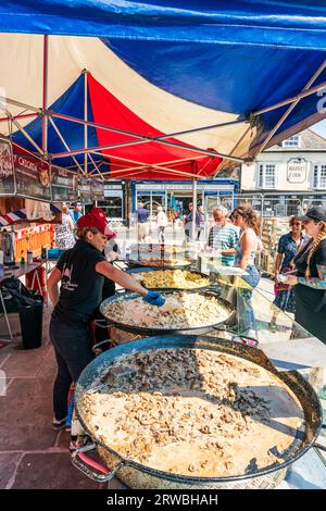 Femme travaillant sur un stand de nourriture française en plein air dans la ville de Sandwich dans le Kent. Comptoir a cinq énormes casseroles d'aliments tels que la tartiflette et la paella. Banque D'Images