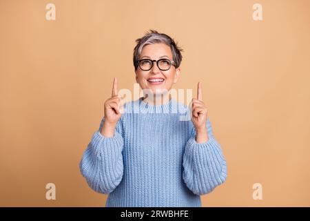 Portrait photo de doigts mignons de grand-mère pointent vers le haut de l'espace vide porter vêtement tricot bleu tendance isolé sur fond de couleur beige Banque D'Images