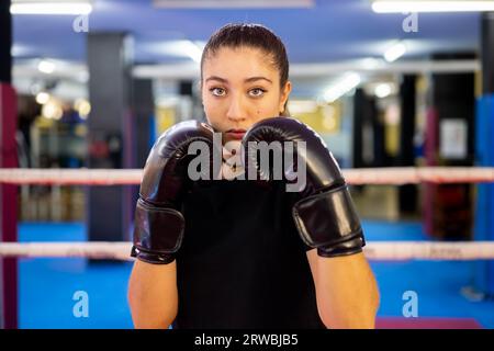 Portrait de boxeur féminin en position de garde dans un ring de boxe. Entraînement aux sports de combat. Rouge et noir. Banque D'Images