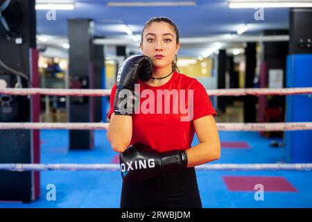 Femme boxer portrait entraînement portant des gants de boxe dans un anneau. Sport de combat. Rouge et noir. Banque D'Images