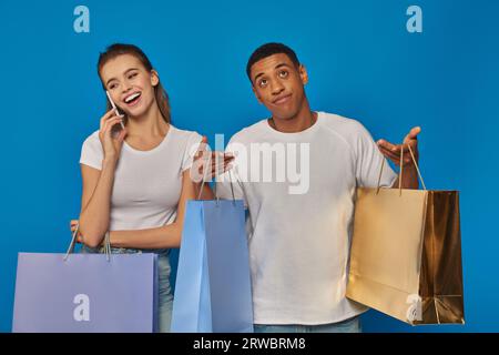 consumérisme, femme heureuse ayant un appel téléphonique tandis que petit ami afro-américain tenant des sacs à provisions Banque D'Images