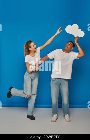 femme avec la main tendue atteignant bulle de pensée près de l'homme afro-américain sur fond bleu, amusant Banque D'Images