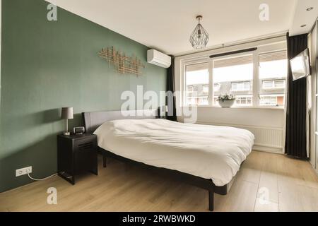 Intérieur de la chambre moderne avec literie blanche et mur vert avec climatiseur à côté de la fenêtre lumineuse dans un appartement spacieux Banque D'Images
