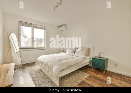 Intérieur de la chambre blanche moderne avec lit confortable et grand miroir à côté de la fenêtre lumineuse dans la maison contemporaine Banque D'Images