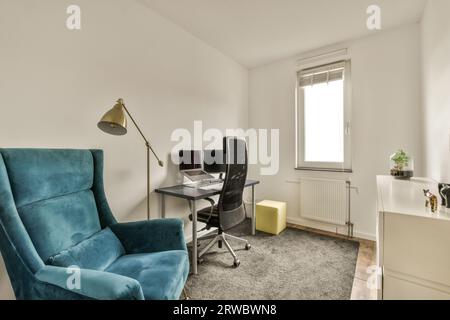 Fauteuil confortable bleu avec ordinateur et ordinateur portable sur le bureau par la fenêtre en face du mur blanc dans l'appartement moderne Banque D'Images