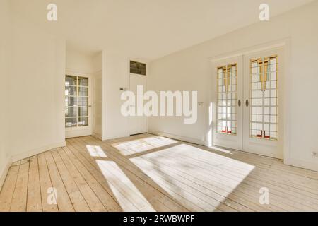 Intérieur d'un appartement spacieux avec la lumière du soleil tombant sur le plancher de bois franc à travers de grandes portes dans une pièce vide avec des murs blancs Banque D'Images