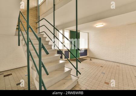 Intérieur de l'immeuble de bureaux avec escalier et garde-corps vert menant à l'étage supérieur contre portes fermées et mur blanc Banque D'Images