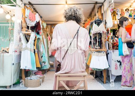 Une femme est assise devant un stand de vêtements au marché hippy Las Dalias à Ibiza, Îles Baléares, Espagne. Banque D'Images