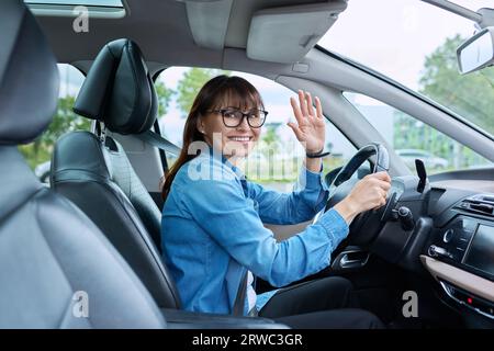 Femme d'âge moyen conducteur assis derrière le volant dans la voiture, souriant regardant la caméra Banque D'Images