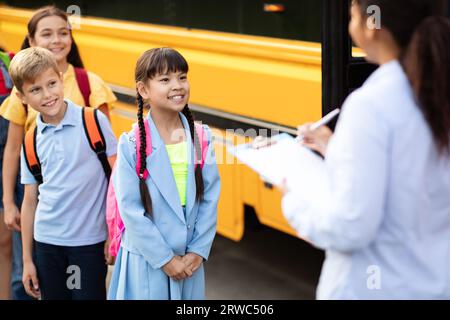 Enseignante noire mettant à jour la liste de contrôle des enfants entrant dans le bus scolaire Banque D'Images