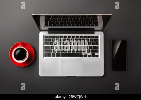 Élégant bureau noir avec ordinateur portable, tasse de café et téléphone portable. Vue de dessus. Banque D'Images