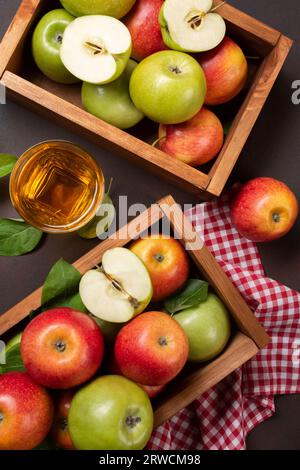 Pommes rouges et vertes mûres dans une boîte en bois avec un verre de jus frais sur fond rouillé. Vue de dessus. Banque D'Images