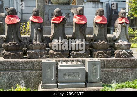 Marqueurs tombaux de style bouddhiste traditionnel avec statues Jizo Bosatsuat et bavettes rouges dans un petit cimetière attaché au temple bouddhiste zen Tengen-ji, dans le district de Yanaka, Taito City, Tokyo, Japon. Banque D'Images