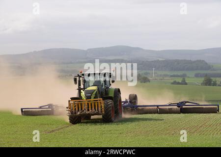 Un tracteur Claas utilisant un Dal-Bo Powerroll 1530 pour rouler un champ d'orge de printemps par temps sec avec vue sur la campagne de l'Aberdeenshire Banque D'Images