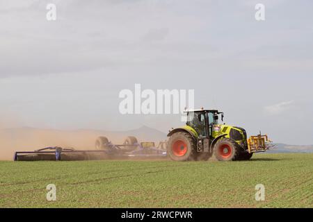 Tracteur Claas Axion 850 remorquant un Dalbo Powerroll 1530 sur un champ d'orge de printemps par temps sec dans l'Aberdeenshire avec vue sur Bennachie Banque D'Images