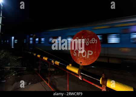 Vieux chemin de fer en Inde, Kerala. Panneau d'arrêt rouillé, long train avec des voitures, barrière de passage à niveau Banque D'Images