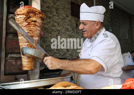 Un chef tranche la viande avec un couteau pour préparer un doner kebab dans un restaurant à Istanbul Banque D'Images