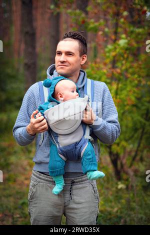 Jeune père avec son bébé nouveau-né dans une écharpe marchant dans la forêt d'automne. Le concept d'une famille heureuse. Banque D'Images