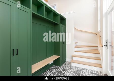 Un grand foyer avec une unité de rangement vert vibrant, un banc et des escaliers en chêne blanc, et un revêtement de sol en carrelage noir et blanc. Banque D'Images